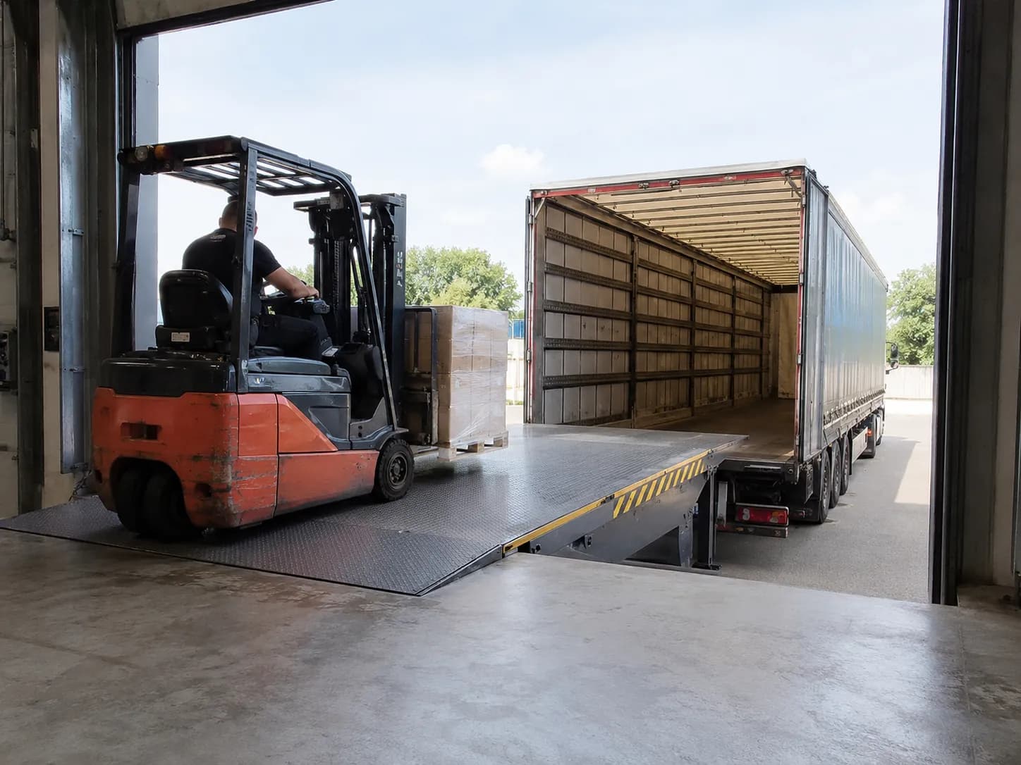 Chariot élévateur chargeant un semi-remorque via un niveleur télescopique
