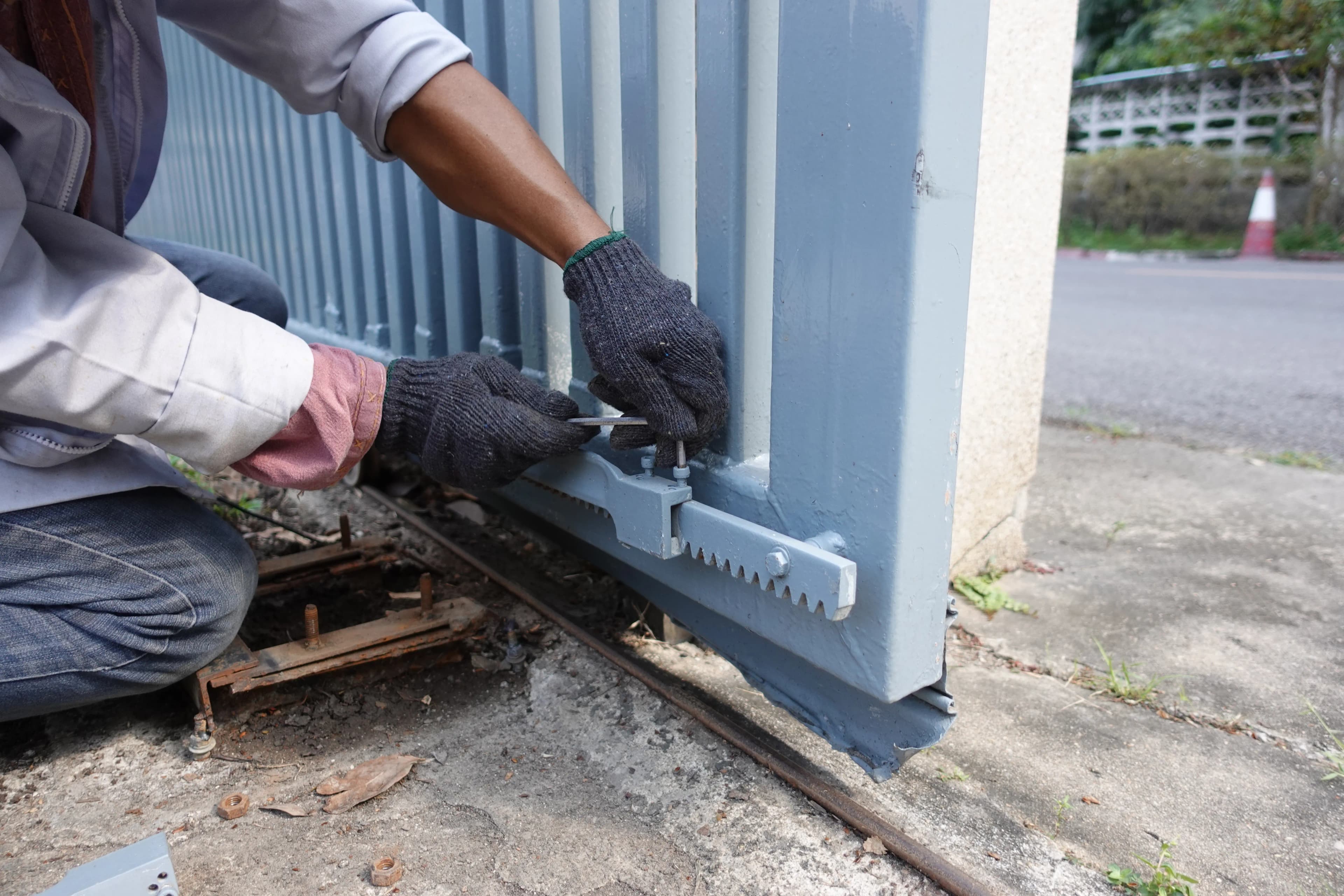 Technicien fixant la crémaillère d'un portail coulissant lors de la pose d'une motorisation